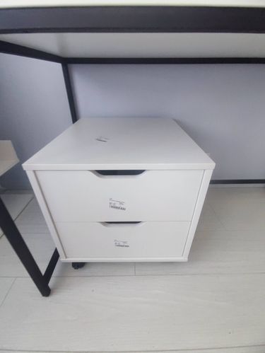 Собран компактный белый ящик с двумя выдвижными секциями на колесиках, установлен под столешницей. Все элементы соединены, конструкция устойчива и готова к использованию.