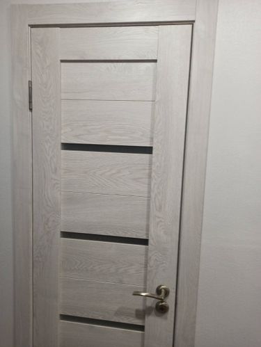 Установлена светлая дверь с горизонтальными вставками, закреплены петли, врезана ручка, отрегулировано полотно для плавного закрывания, обеспечена надежная фиксация в проеме.