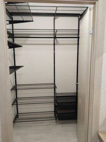 Установлены металлические стеллажи в нише, закреплены на стене. Полки ровно выровнены, обеспечивая надежность и устойчивость конструкции для хранения вещей.