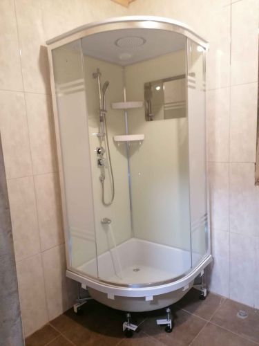 Установлена современная душевая кабина с полукруглыми стеклянными дверцами, поддон надежно закреплен, подключены водопроводные коммуникации, добавлены полки для удобства.