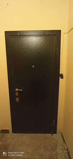 Установлена металлическая дверь с замками и ручкой, закреплена в проеме, обеспечивая надежную защиту. Завершены отделочные работы вокруг конструкции, обеспечивая эстетичный вид.