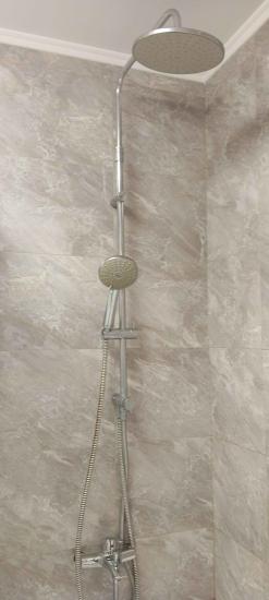 Установлен новый душевой комплект с верхним и ручным распылителями, подключены шланги, закреплены крепления на стене, проверена герметичность соединений, обеспечена функциональность системы.