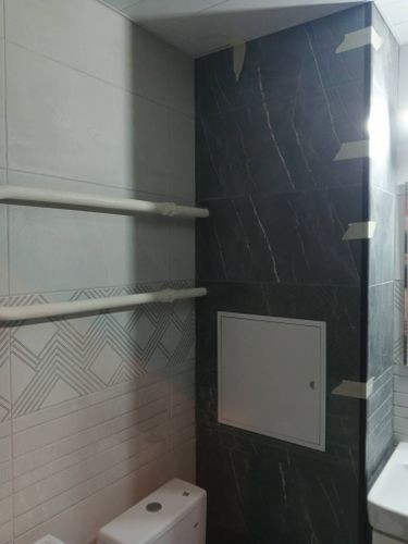 Установлены керамические плиты на стенах ванной комнаты, включая сложные участки вокруг труб и люка. Использованы разные текстуры и оттенки для создания стильного и современного интерьера.