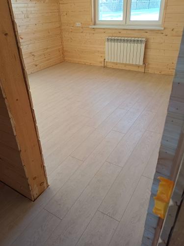 Покрытие пола завершено: панели уложены ровно, без зазоров, создавая гладкую поверхность. Цвет светлый, гармонирует с деревянными стенами, создавая уютную атмосферу в помещении.