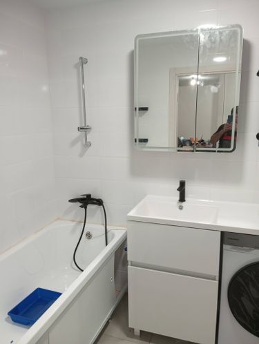 Изображение ванной комнаты с белой плиткой, ванной, раковиной с зеркалом и стиральной машиной. Установлены сантехника и мебель, чистый и аккуратный интерьер.