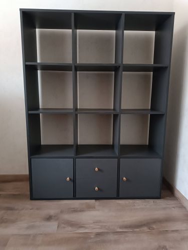 Собран стеллаж с девятью секциями и тремя ящиками, установлены ручки. Конструкция надежно закреплена, все детали подогнаны точно, обеспечивая устойчивость и функциональность.