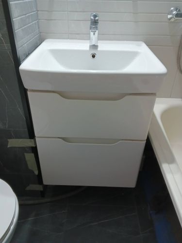 На полу и стенах ванной комнаты уложена керамическая плитка. Поверхности ровные, швы аккуратно заполнены затиркой. Установлена раковина с тумбой, подключен смеситель.