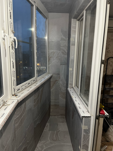 Выполнена облицовка стен и потолка балкона ПВХ панелями серого цвета с текстурой камня. Установлены новые пластиковые окна, подоконники и откосы. Все элементы аккуратно подогнаны.