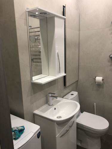 Изображение ванной комнаты с раковиной, зеркальным шкафом, унитазом и полотенцесушителем. На стиральной машине лежит полотенце. Светлые стены и современный дизайн.