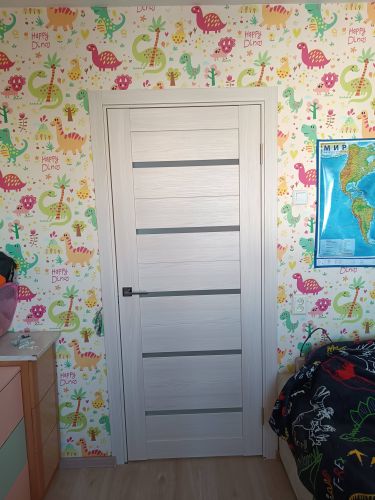 Установлена светлая деревянная дверь с горизонтальными вставками, аккуратно закреплена в проеме, оснащена ручкой и петлями, идеально вписана в интерьер комнаты с яркими обоями.