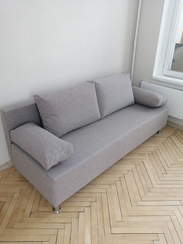 Собран диван: установлены ножки, закреплены подлокотники, прикреплены спинка и сиденье, добавлены подушки. Готовое изделие стоит на паркете у стены.