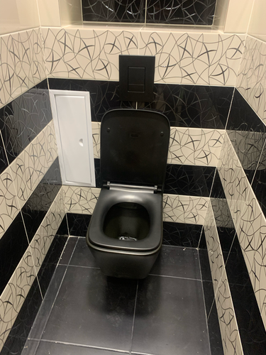 Установлен подвесной унитаз с черной панелью на кафельной стене. Подключены коммуникации, закреплена конструкция, обеспечена надежная фиксация и герметичность. Завершена облицовка плиткой.