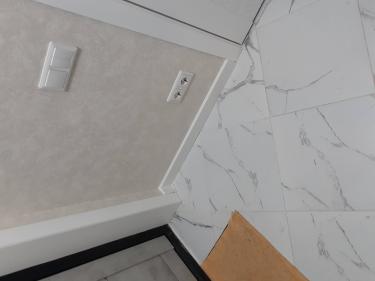 Установлен белый плинтус на стыке стены и пола, обеспечивая аккуратный переход между поверхностями. Завершён монтаж, все элементы плотно прилегают, создавая гармоничный вид интерьера.