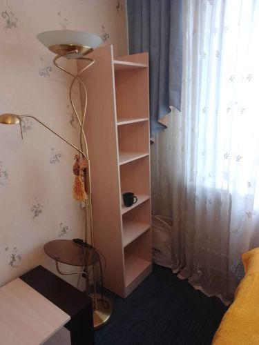 Установлен книжный стеллаж с четырьмя полками в углу комнаты. Элемент мебели аккуратно вписан в интерьер, обеспечивая дополнительное место для хранения.