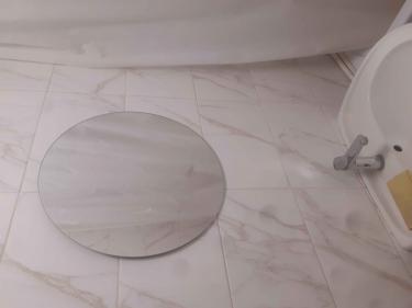 Круглое зеркало аккуратно закреплено на стене из плитки в ванной комнате, расположено над раковиной. Работа выполнена с точностью, без видимых креплений, создавая чистый и элегантный вид.