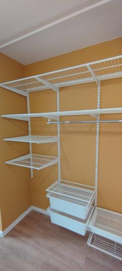 Изображение демонстрирует установленную систему полок в углу комнаты. Белые металлические конструкции крепко зафиксированы на стене, обеспечивая организованное хранение.