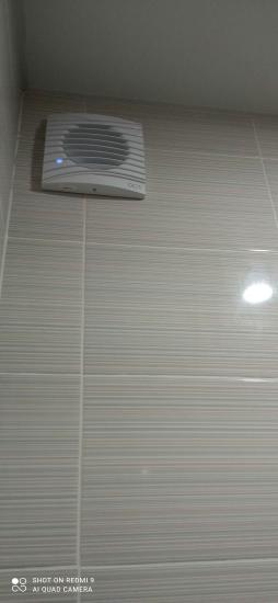 Установлен вентилятор на стене с плиткой, подключен к электросети, обеспечивая циркуляцию воздуха в помещении. Завершён монтаж, проверена работоспособность устройства.