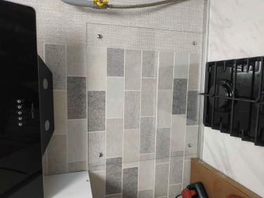 Изображение демонстрирует обновлённую кухню с новой плиткой на стене и установленной вытяжкой над плитой. Видна часть газовой трубы и инструменты на столешнице.