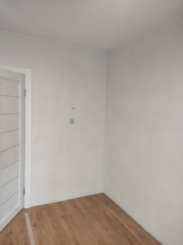 Изображение демонстрирует пустую комнату с белыми стенами и деревянным полом после завершения работ. Стены подготовлены для дальнейших действий, поверхность ровная и гладкая.