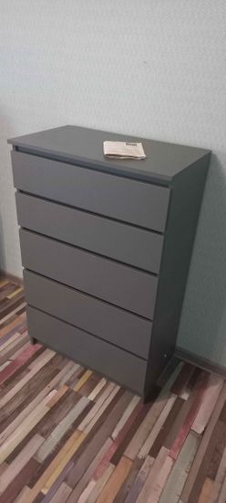 Собран новый предмет мебели с пятью ящиками, установлен на ровной поверхности. Все детали аккуратно соединены, обеспечивая устойчивость и функциональность конструкции.