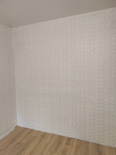 На стену аккуратно наклеены фотообои с нежным узором. Поверхность ровная, без дефектов и пузырей. Края тщательно подогнаны, создавая целостный вид. Пол завершает гармоничную композицию.