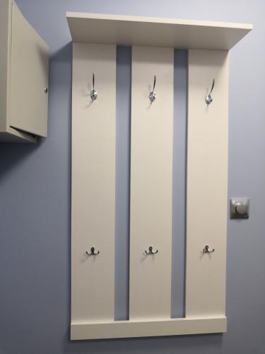 На стене закреплена белая вешалка с полкой и крючками, обеспечивающая удобное хранение одежды. Установка завершена, элементы надежно зафиксированы.