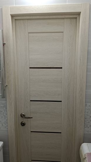 Установлена светлая межкомнатная дверь с фурнитурой, ручка и замок закреплены, коробка выровнена, наличники подогнаны, конструкция надежно зафиксирована, зазоры устранены.