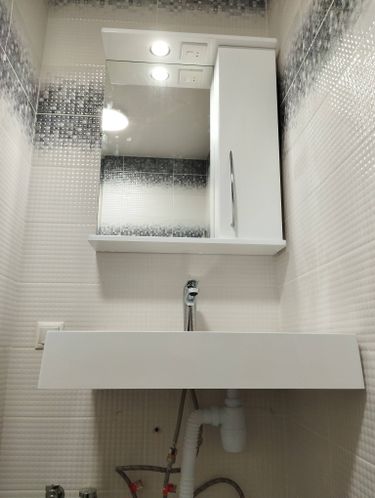 Установлена новая раковина, подключены трубы, смеситель закреплён, проверена герметичность соединений, обновлено зеркало с подсветкой, добавлены розетки, завершена отделка плиткой.