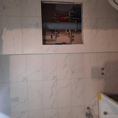 Отделка завершена: кафель ровно уложен на стену, швы аккуратно затерты, сантехнические трубы закрыты плиткой, оставлено отверстие для доступа к коммуникациям.