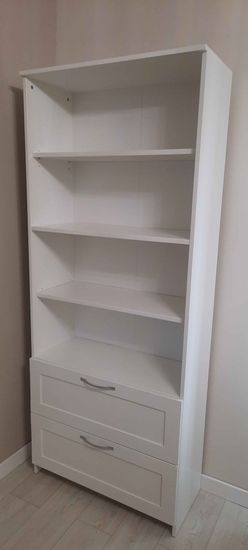 Собран белый стеллаж с полками и двумя выдвижными ящиками. Конструкция установлена на ровный пол, обеспечена устойчивость и надежность. Все элементы аккуратно подогнаны и закреплены.