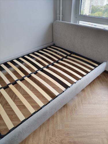 Изображена собранная кровать с деревянными ламелями на каркасе, установленная на паркетном полу у окна.