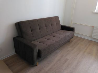 Собран диван: установлены ножки, прикреплены подлокотники, закреплена спинка, проверена устойчивость. Готов к использованию, стоит на месте, все элементы на своих позициях.