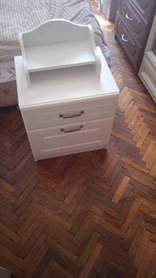 Собран белый комод с двумя ящиками и декоративной полкой сверху. Установлены ручки, выровнены детали, обеспечена устойчивость конструкции на паркете.
