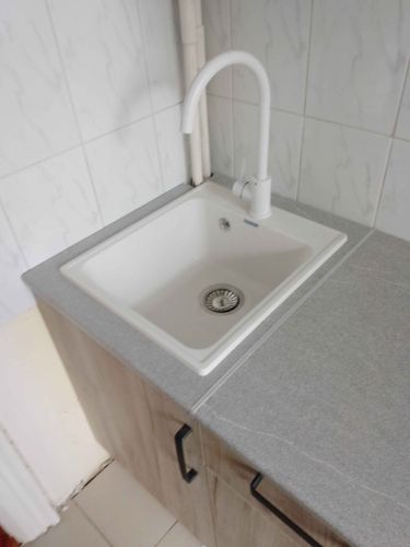 Установлен новый белый кран на кухонную раковину, подключены водопроводные трубы, проверена герметичность соединений. Работы завершены, система функционирует без утечек.