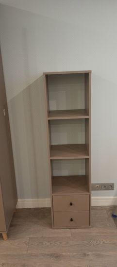 Собран новый стеллаж с четырьмя полками и двумя ящиками. Установлен на ровный пол, закреплён для устойчивости. Все детали соединены, конструкция готова к использованию.