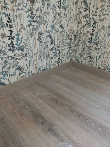 На полу уложено новое покрытие, тщательно подогнанное по краям. Установлены плинтусы, создающие аккуратный и завершенный вид. Поверхность ровная, без видимых дефектов.