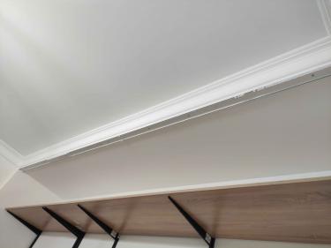 Установлен белый декоративный элемент вдоль стыка стен и потолка, аккуратно закреплённый, без зазоров и неровностей, создающий завершённый вид интерьера.