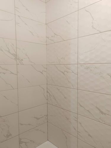 На стенах ровно уложена керамическая облицовка с мраморным узором. Швы аккуратно заполнены, поверхность гладкая, без дефектов. Работа завершена, результат эстетичный и прочный.