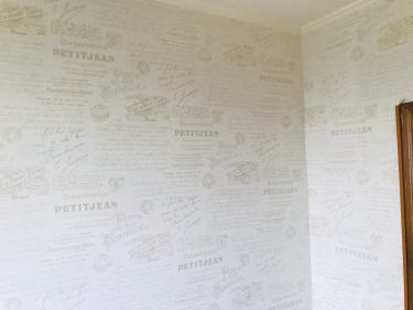 На стенах аккуратно наклеены обои с текстовым узором, создавая стильный и гармоничный интерьер. Поверхность ровная, без видимых швов и пузырей, обеспечивая качественный результат.