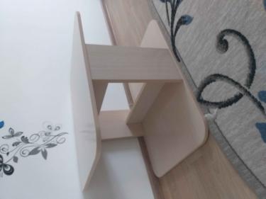 Изображен обновленный столик с деревянной поверхностью на фоне светлой стены с узором. Пол светлый, на ковре цветочный орнамент.