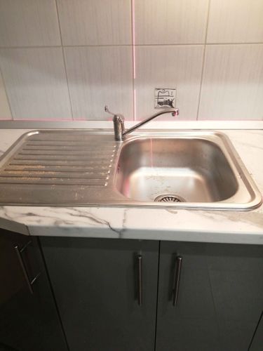 Изображение кухонной мойки с мраморной столешницей, встроенной раковиной и краном на фоне плитки. Видны лазерные линии для выравнивания.