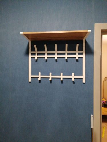 Установлена деревянная полка на синей стене с металлическими кронштейнами и крючками для одежды. Работа завершена аккуратно и надежно, конструкция закреплена ровно и прочно.