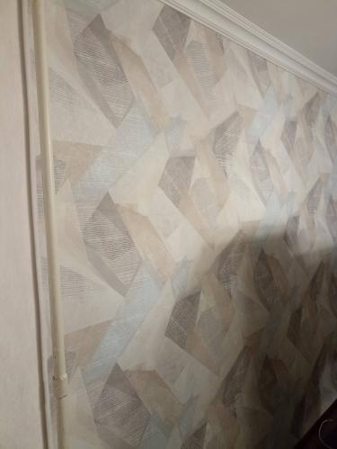 Стены покрыты новыми обоями с геометрическим узором, аккуратно выровнены, без видимых стыков и пузырей. Углы и края обработаны тщательно, создавая единое целое.