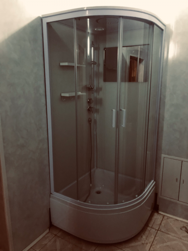 Установлена современная душевая конструкция с прозрачными дверцами и встроенными полками. Подключены водопроводные коммуникации, проверена герметичность, завершена отделка стен.