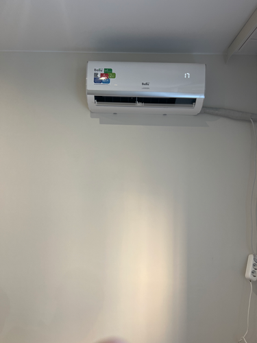 Изображен установленный кондиционер на стене, подключенный к электросети. Завершены работы по размещению устройства, обеспечено его функционирование и надежное крепление.