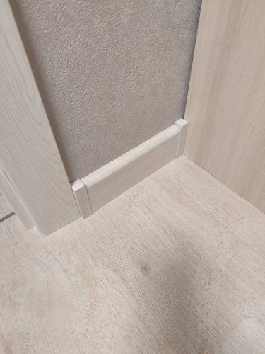 Угловое соединение плинтуса выполнено аккуратно, детали подогнаны точно. Установлены заглушки, обеспечивающие завершённый вид. Плинтус плотно прилегает к стене и полу, создавая гармоничный переход.