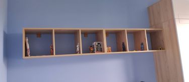 Установлена деревянная конструкция на стене, закреплена крепежами. Полка ровно размещена, выдерживает вес предметов. Эстетично дополнена фигурками и коробками, гармонично вписывается в интерьер.