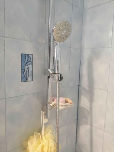 Изображение демонстрирует установленный новый душевой комплект с лейкой и шлангом. На стене плитка с декоративным элементом. Рядом мыльница с аксессуарами.