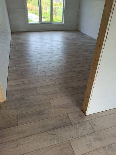 В комнате уложено напольное покрытие, панели ровно подогнаны, создавая гладкую поверхность. Цвет древесины гармонирует с интерьером, обеспечивая уют и стильное оформление пространства.