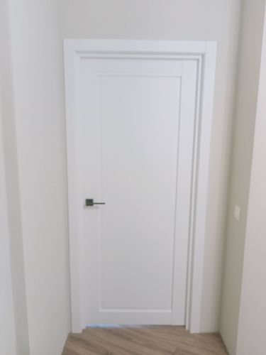 Установлена белая дверь с ручкой, выполнена подгонка полотна, закреплены петли, отрегулированы замки, оформлен дверной проем, установлены наличники, обеспечена плавность открывания.